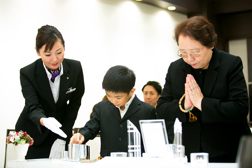 葬儀中に、葬儀スタッフが子供に、お焼香のやり方を案内している様子