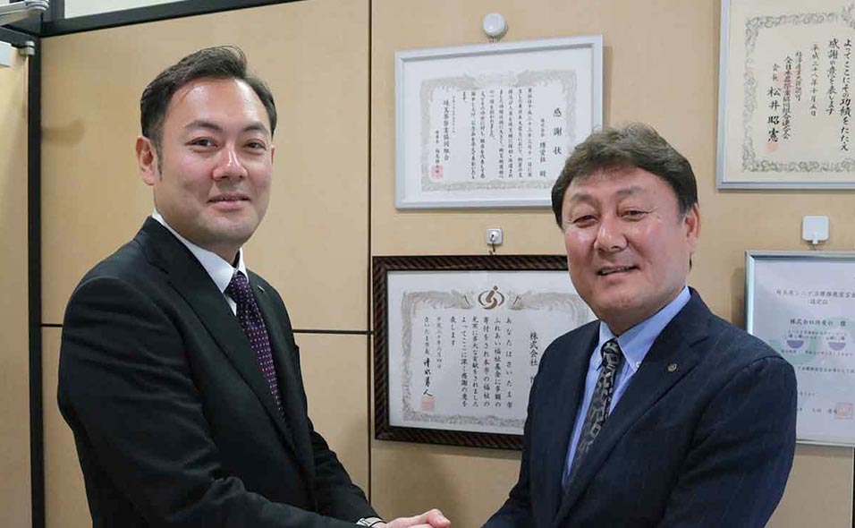 代表取締役 会長：村上 基一と代表取締役 社長：村上 武白が手を取り合っている様子
